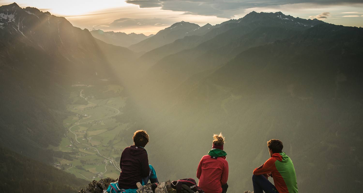 Drei Personen bewundern das Panorama bei Sonnenaufgang auf einer Bergspitze im Pustertal