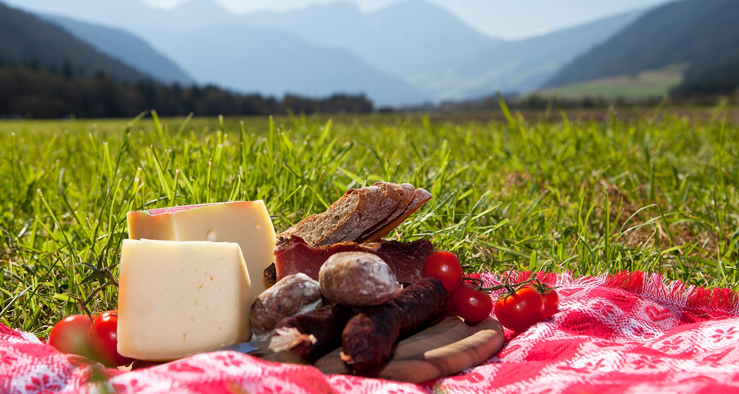 Nahaufnahme eines ausgebreiteten Picknickkorb-Inhaltes mit Käse, Wurt, Speck und Kirschtomaten