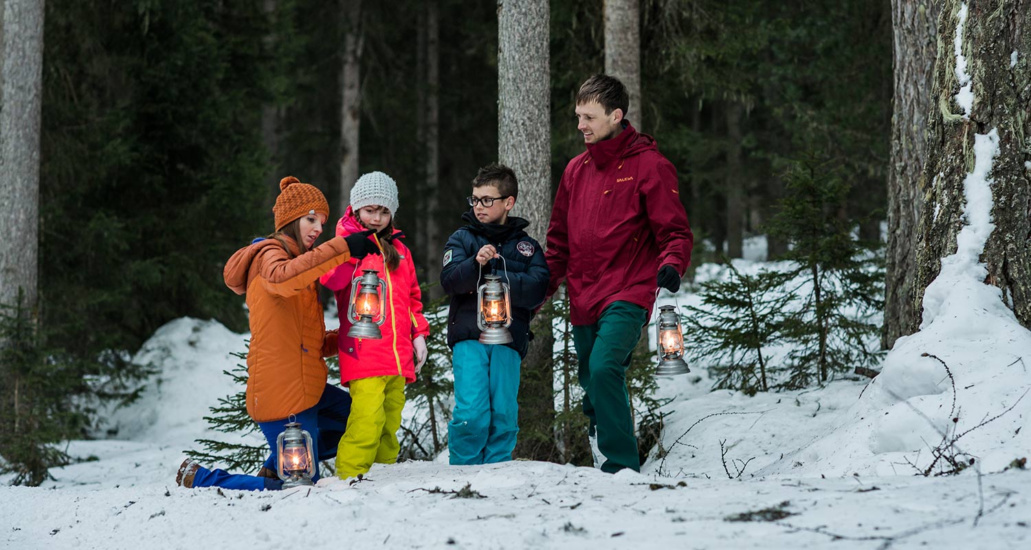 Kinder in Winterkleidung mit einer Laterne im schneebedeckten Wald