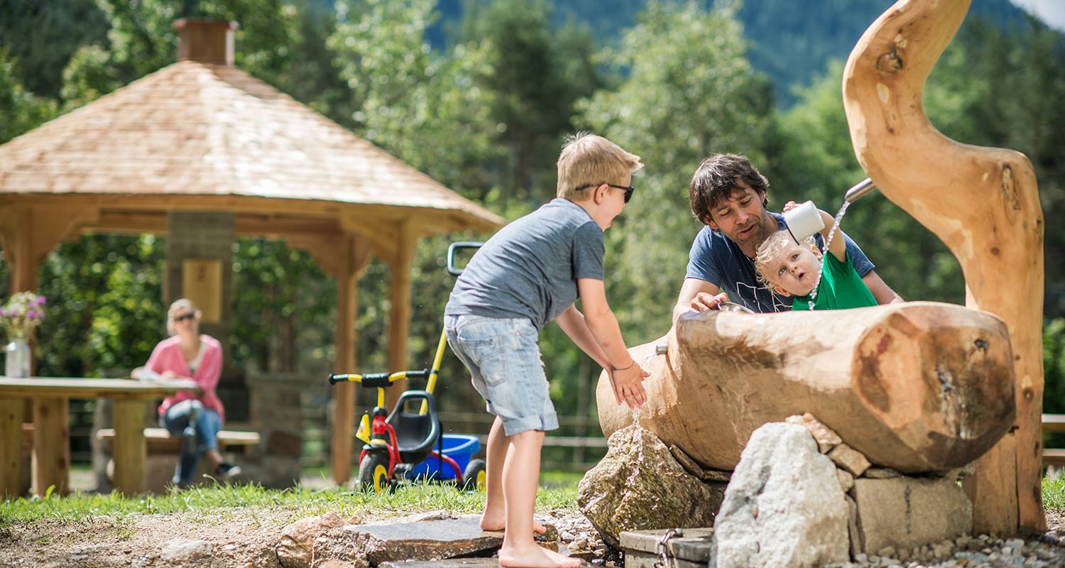 Familie rund um einem Holzbrunnen im Freien an einem Sommertag
