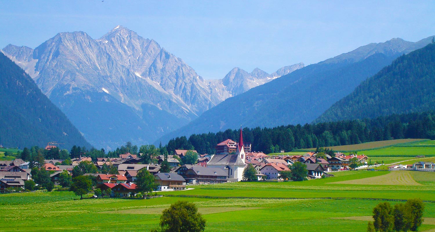 Vista della località Rasen in estate con verdi prati e montagne sullo sfondo