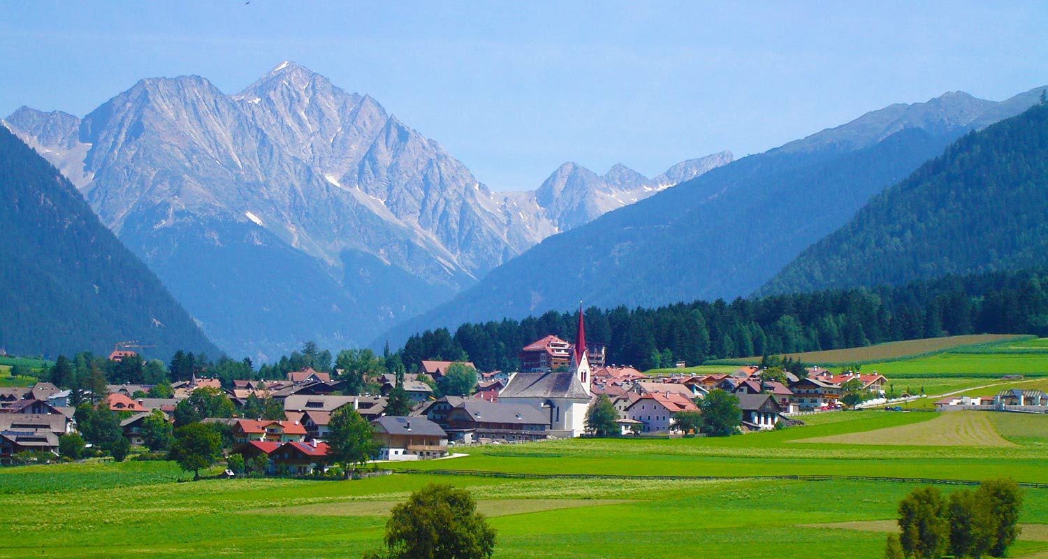 Blick auf den Ort Rasen im Sommer mit grüner Wiese und Bergen im Hintergrund