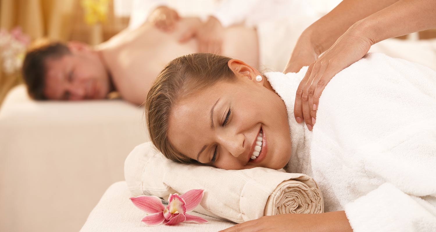 Frau genießt eine Massage und Mann auf Massagebett im Hintergrund