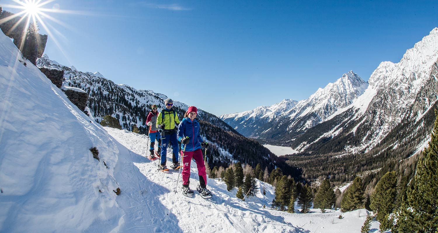 Drei junge Schneeschuhwanderer spazieren lachend einen Bergweg entlang
