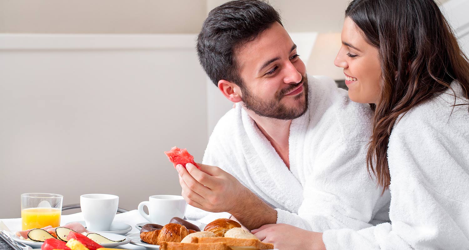 Paar im Bademantel beim Frühstück im Hotelzimmer